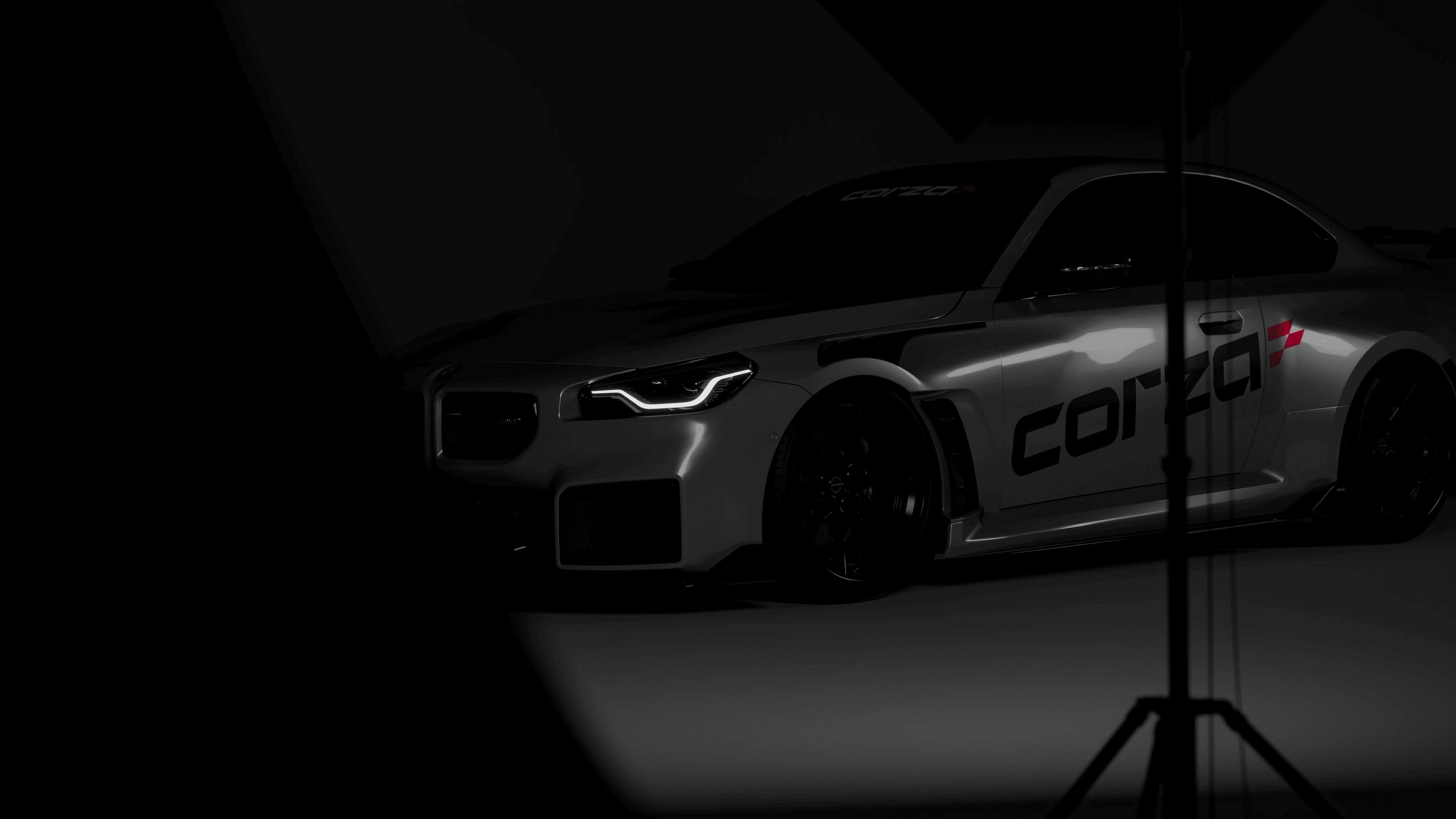 A silver sports car with "corza" branding is partially illuminated in a dark studio, with lighting equipment visible in the foreground.