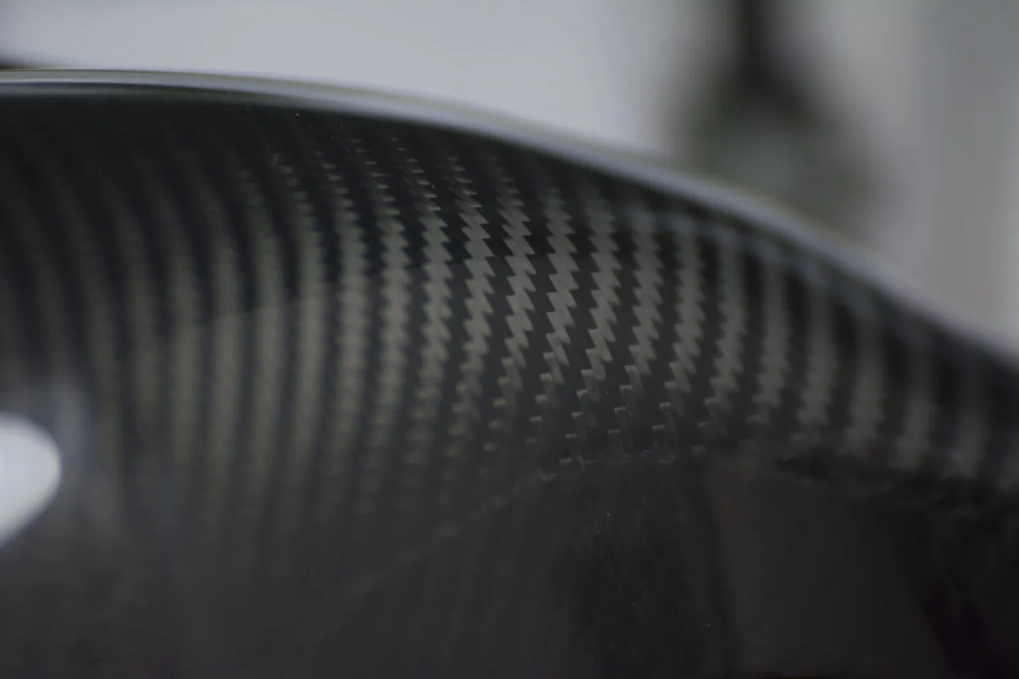 Close-up of a curved surface with a carbon fiber pattern, showing a glossy finish and a reflection of light.